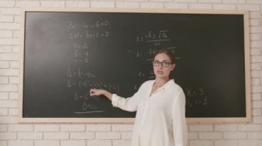 Okul öğretmeni sınıfta gençlerle konuşuyor. Öğrencilere ders vermek ve tahtayı silmek için sınıfın önünde duran kadın üniversite öğretmeni. Eğitim kavramı.