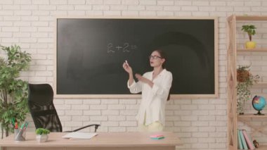 Okul öğretmeni sınıfta gençlerle konuşuyor. Kadın üniversite öğretmeni sınıfın önünde duruyor ve öğrencilere temel matematik dersini anlatıyor. Eğitim kavramı.