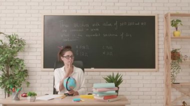 Sınıfta öğretmen çalışma günü. Komik saç stili olan karizmatik kadın üniversite öğretmeni sınıfta oturmuş dünyayı döndürüyor ve tatil için ülke seçiyor. Eğitim kavramı.