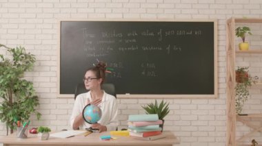 Sınıfta öğretmen çalışma günü. Komik saç stili olan karizmatik kadın üniversite öğretmeni sınıfta oturmuş dünyayı döndürüyor ve tatil için ülke seçiyor. Eğitim kavramı.