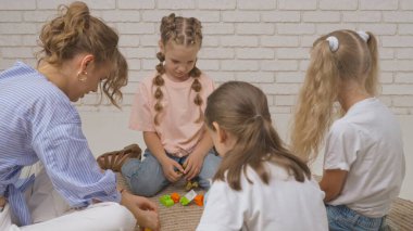Anaokulu derslerini ziyaret eden bir grup çocuk. Genç bayan öğretmen ve bir grup çocuk yerde oturup gelişim derslerinde oyuncakçılık oynuyorlar. Çocuk eğitimi konsepti.