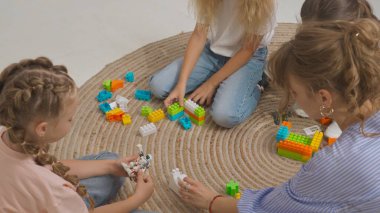 Anaokulu derslerini ziyaret eden bir grup çocuk. Genç bayan öğretmen ve bir grup çocuk yerde oturup gelişim derslerinde oyuncakçılık oynuyorlar. Çocuk eğitimi konsepti.