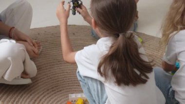 Anaokulu derslerini ziyaret eden bir grup çocuk. Genç öğretmen ve bir grup çocuk yerde oturup gelişim derslerinde oyuncakçılık oynuyorlar. Çocuk eğitimi konsepti. Yavaş çekim.