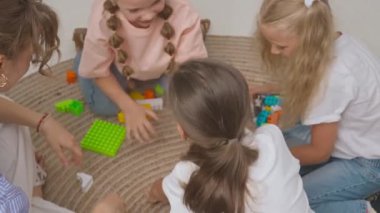 Anaokulu derslerini ziyaret eden bir grup çocuk. Genç öğretmen ve bir grup çocuk yerde oturup gelişim derslerinde oyuncakçılık oynuyorlar. Çocuk eğitimi konsepti. Yavaş çekim.