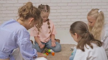 Anaokulu derslerini ziyaret eden bir grup çocuk. Genç öğretmen ve bir grup çocuk yerde oturup gelişim derslerinde oyuncakçılık oynuyorlar. Çocuk eğitimi konsepti. Yavaş çekim.