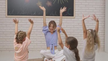 Anaokulu derslerini ziyaret eden bir grup çocuk. Genç öğretmen ve bir grup çocuk gelişim sınıfında el sallayarak ve el çırparak eğleniyorlar. Çocuk eğitimi konsepti. Yavaş çekim.
