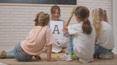 Anaokulu derslerini ziyaret eden bir grup çocuk. Genç bayan öğretmen ve bir grup çocuk gelişim derslerinde yaratıcı görevler yapıyor, alfabe öğreniyorlar. Çocuk eğitimi konsepti.