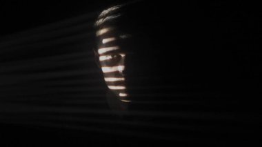 Bir adam yatay ışık şeritleriyle kısmen aydınlanarak dramatik gölgelerle yüzleşir. Karanlıkta bir adamın silueti. Aydınlık ve karanlık oyunu.