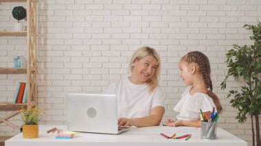 Küçük kız okula ya da anaokuluna gidiyor. Yetişkin kadın, anne ve küçük kız oturma odasında, annesi laptopta çalışıyor, kız konuşmaya geliyor, sarılıyor ve annesini öpüyor..