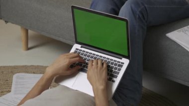 Evde okuyan genç bir öğrenci. Odaklanmış yetişkin üniversite öğrencisi dizüstü bilgisayarlı yeşil ekranla yerde yatıp klavyede ödev testi yapıyor. Eğitim kavramı.