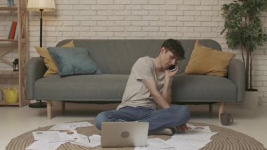 Evde okuyan genç bir öğrenci. Genç bir üniversite öğrencisi bir odada oturuyor, ödev yapıyor ya da sınavlara çalışıyor. Genç bir erkek öğrenci akıllı bir telefonla konuşuyor. Eğitim kavramı.