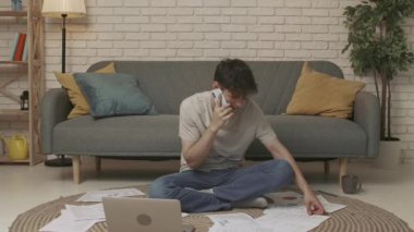Evde okuyan genç bir öğrenci. Genç bir üniversite öğrencisi bir odada oturuyor, ödev yapıyor ya da sınavlara çalışıyor. Genç bir erkek öğrenci akıllı bir telefonla konuşuyor. Eğitim kavramı.