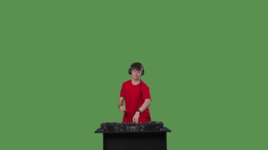 DJ masasının arkasında ustaca müziği karıştıran parlak kırmızı tişört giymiş erkek DJ, canlı müzik etkinliğinin yüksek enerjili atmosferini aktarıyor. Yeşil ekran krom anahtarı