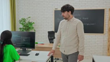 Bir öğretmen modern bir sınıf ortamında bir Python programlama projesinde çalışan bir öğrenciye dikkatle yardım eder. Kişisel rehberlik öğrencinin karmaşık kodlama sorunlarını çözmesine yardımcı olur.