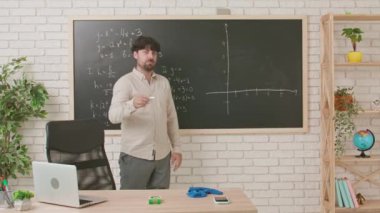 Bir erkek öğretmen geometri dersi veriyor ve sınıfta tahtaya yazılmış bir görevi anlatıyor. Eğitim anlayışı, bir okulda veya üniversitede öğretmenlik.