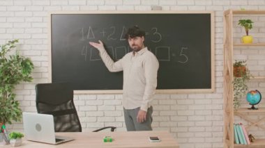 Erkek bir öğretmen matematik dersi veriyor ve tahtaya yazılmış denklemleri açıklıyor. Eğitim anlayışı, bir okulda veya üniversitede öğretmenlik.