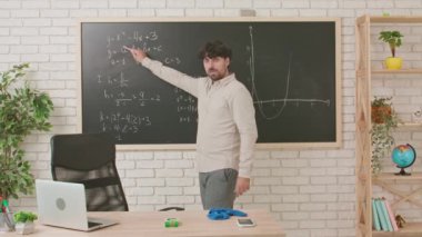 Bir erkek öğretmen geometri dersi veriyor ve sınıfta tahtaya yazılmış bir görevi anlatıyor. Eğitim anlayışı, bir okulda veya üniversitede öğretmenlik.