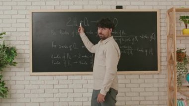 Erkek bir öğretmen kimya dersi veriyor ve sınıfta tahtaya yazılmış bir ödevi anlatıyor. Eğitim anlayışı, bir okulda veya üniversitede öğretmenlik.