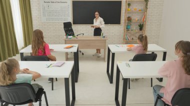 İlkokul çocukları fen bilgisi öğreniyor. Ortaokul öğrencileri fen bilimleri kimyası dersinde. Öğretmen çocuklarla konuşuyor, test tüpleri ve masada sıvı var..