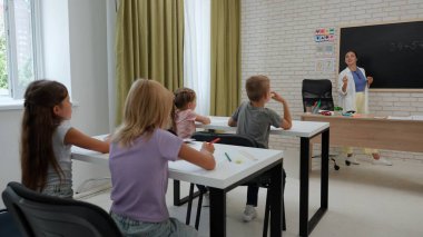 Bir grup ilkokul öğrencisi. Sınıftaki ortaokul öğrencileri, kadın öğretmen çocuklara ders veriyor, tahtaya matematik örneği yazıyor, sorular soruyor. İlkokul.