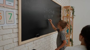Bir grup ilkokul öğrencisi. Sınıftaki ortaokul öğrencileri, kadın öğretmen çocuklara ders veriyor, çocuk tahtaya matematik örneği yazıyor. İlkokul.