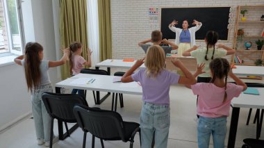 Bir grup ilkokul öğrencisi. Sınıftaki ortaokul öğrencileri, kadın öğretmen ve çocuklar ders sırasında ısınma egzersizleri yapıyorlar. İlkokul.