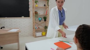 Bir grup ilkokul öğrencisi. Sınıftaki ortaokul öğrencileri, kadın öğretmenler çocuklara ders veriyor. Masaları düzenlemeye yardım eden çocuklarla konuşuyorlar. İlkokul.
