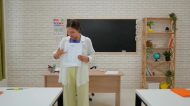 Bir grup ilkokul öğrencisi. Sınıftaki ortaokul öğrencileri, kadın öğretmen çocuklara ders veriyor, çocuklara ödevleri olan kağıt çarşaf veriyorlar. İlkokul.