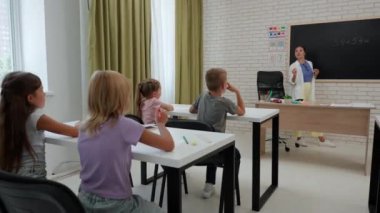 Bir grup ilkokul öğrencisi. Sınıftaki ortaokul öğrencileri, kadın öğretmen çocuklara ders veriyor, tahtaya matematik örneği yazıyor, sorular soruyor. İlkokul.