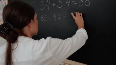 Bir grup ilkokul öğrencisi. Sınıftaki ortaokul öğrencileri, kadın öğretmen çocuklara ders veriyor, çocuğun tahtaya cevap yazmasına yardım ediyor. İlkokul.