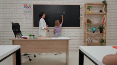 Bir grup ilkokul öğrencisi. Sınıftaki ortaokul öğrencileri, kadın öğretmen çocuklara ders veriyor, kız tahtaya doğru cevabı yazıyor. İlkokul.