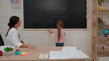 Bir grup ilkokul öğrencisi. Sınıftaki ortaokul öğrencileri, kadın öğretmen çocuklara ders veriyor, küçük kız tahtada matematik örneği alıyor. İlkokul.