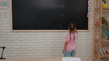 Bir grup ilkokul öğrencisi. Sınıftaki ortaokul öğrencileri, kadın öğretmen çocuklara ders veriyor, kız tahtaya matematik örneği yazıyor, cevabı siliyor. İlkokul.
