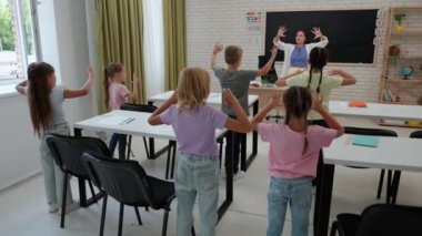 Bir grup ilkokul öğrencisi. Sınıftaki ortaokul öğrencileri, kadın öğretmen ve çocuklar ders sırasında ısınma egzersizleri yapıyorlar. İlkokul.