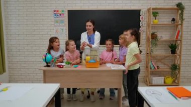 Bir grup ilkokul öğrencisi. Sınıftaki ortaokul çocukları, kadın öğretmen ve çocuklar, sınıfın köşesinde bir hamster 'a bakıyorlar, küçük bir hayvanı tutan özel öğretmen. İlkokul.