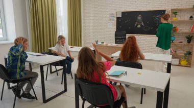 Bir grup ilkokul öğrencisi sınıfta fen bilgisi öğreniyor. Ortaokul öğrencileri ve kızlar astronomi sınıfında oturuyor. Çocuklar derste eğleniyor, konuşuyor ve şakalaşıyorlar. Modern eğitim kavramı.