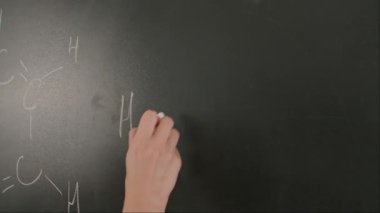 Bayan öğretmenin elinde tebeşir var. Karatahtaya kadın el yazısı formülleri yazmaya yakın bir yerde profesör tahtaya ya da öğrenci çözme görevine yazı yazıyor. Eğitim ve bilim konsepti.