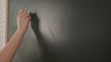 Bayan öğretmenin elinde tebeşir var. Karatahtaya kadın el yazısı formülleri yazmaya yakın bir yerde profesör tahtaya ya da öğrenci çözme görevine yazı yazıyor. Eğitim ve bilim konsepti.