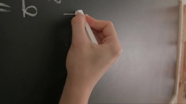 Bayan öğretmenin elinde tebeşir var. Karatahtaya kadın el yazısı rakamlarını ve formüllerini kapatan profesör, tahtaya ya da öğrenci çözme görevine yazı yazıyor. Eğitim ve bilim konsepti.