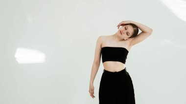 Siyah elbiseli genç kadın beyaz arka planda çağdaş dans ediyor..