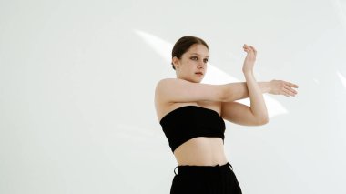 Siyah elbiseli genç kadın beyaz arka planda çağdaş dans ediyor..