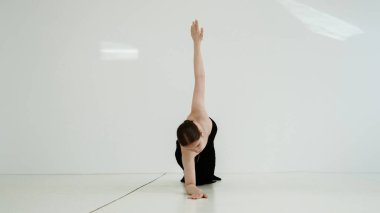 Siyah elbiseli genç kadın beyaz arka planda çağdaş dans ediyor..