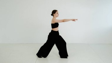 Siyah elbiseli genç kadın beyaz arka planda çağdaş dans ediyor..