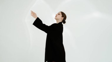 Siyah elbiseli genç kadın beyaz arka planda çağdaş dans ediyor..