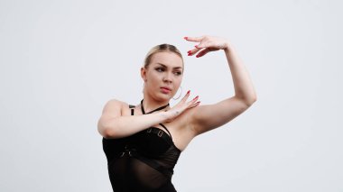 Siyah elbiseli genç bir kadın beyaz arka planda yüksek tepelerde dans ediyor..