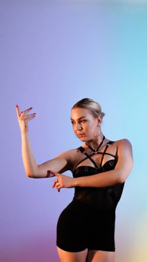 Siyah elbiseli genç bir kadın çok renkli bir odada yüksek tepelerde dans ediyor..