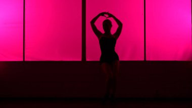 Pembe ışıkla yüksek tepelerde dans eden bir kadının silüeti..