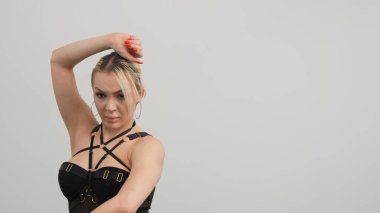 Siyah elbiseli genç bir kadın beyaz arka planda yüksek tepelerde dans ediyor..