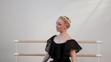 Siyah elbiseli güzel bir balerin, beyaz güneşli bir odada dans eder. Siyah bir zemin de bir bale barının yanında.