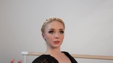 Siyah elbiseli güzel bir balerin, beyaz güneşli bir odada dans eder. Siyah bir zemin de bir bale barının yanında.